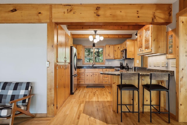 kitchen with kitchen peninsula, stainless steel fridge, beam ceiling, light hardwood / wood-style flooring, and a breakfast bar area