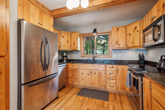 kitchen featuring light wood-type flooring, dark stone counters, a textured ceiling, stainless steel appliances, and sink