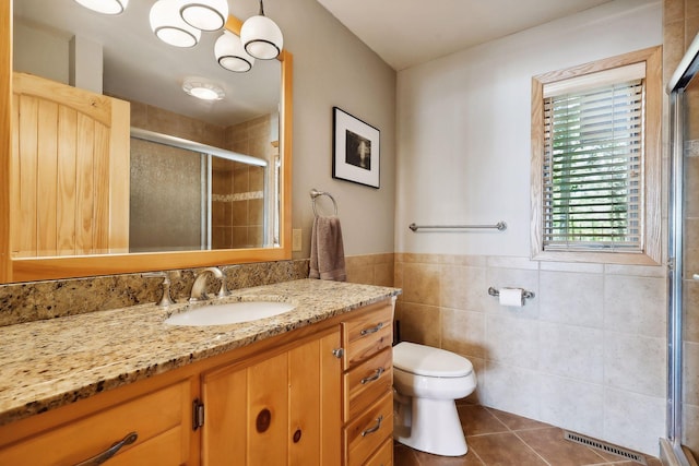 bathroom featuring tile patterned floors, an enclosed shower, toilet, vanity, and tile walls