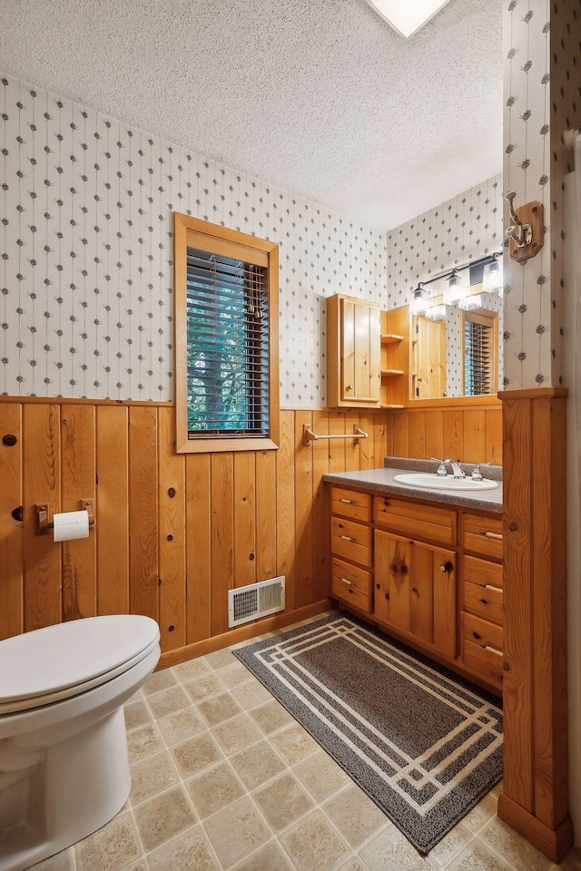 bathroom with vanity, wood walls, toilet, and a textured ceiling