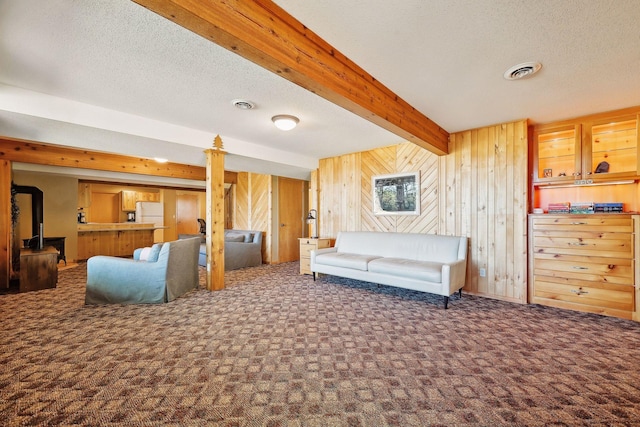 living room featuring beamed ceiling, wood walls, a textured ceiling, and dark colored carpet