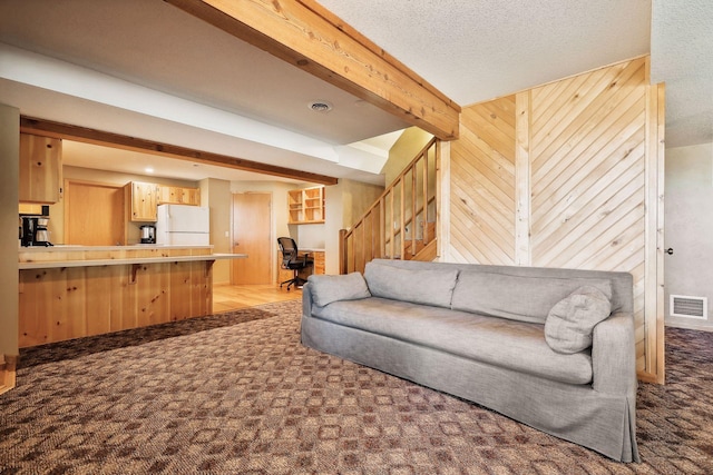 living room with carpet flooring, wood walls, beamed ceiling, and a textured ceiling