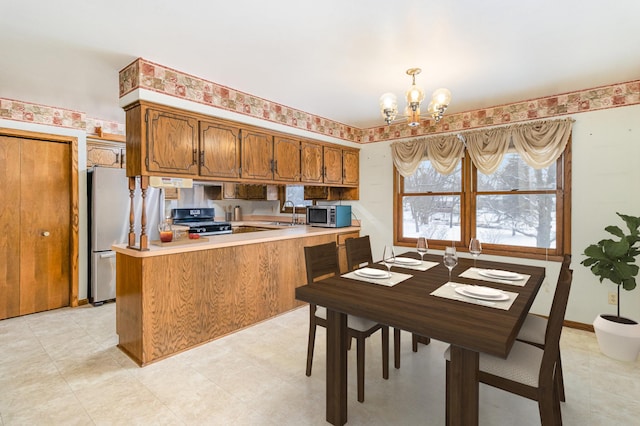 kitchen with kitchen peninsula, decorative light fixtures, stainless steel appliances, an inviting chandelier, and sink