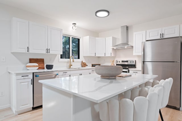 kitchen featuring a center island, wall chimney range hood, sink, appliances with stainless steel finishes, and white cabinetry