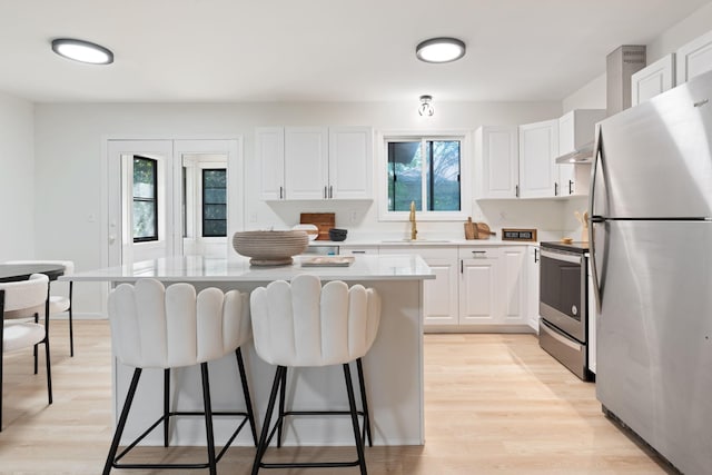 kitchen with appliances with stainless steel finishes, sink, light hardwood / wood-style flooring, a center island, and white cabinetry