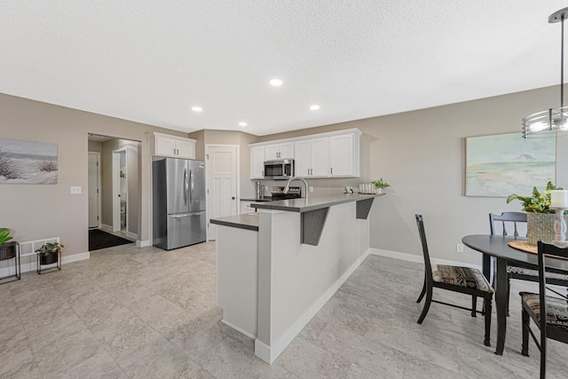 kitchen featuring kitchen peninsula, a textured ceiling, stainless steel appliances, pendant lighting, and white cabinetry