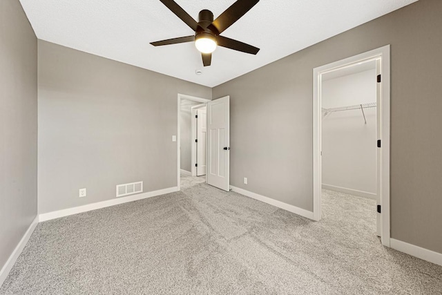 unfurnished bedroom featuring a walk in closet, ceiling fan, a closet, and light carpet