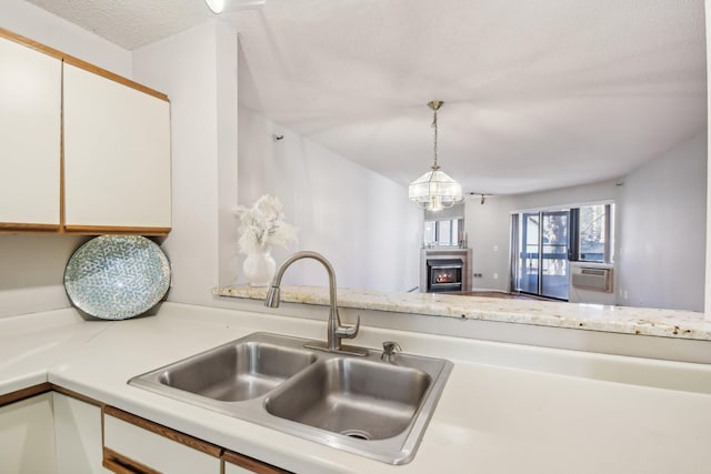 kitchen featuring a fireplace, a textured ceiling, sink, pendant lighting, and white cabinets