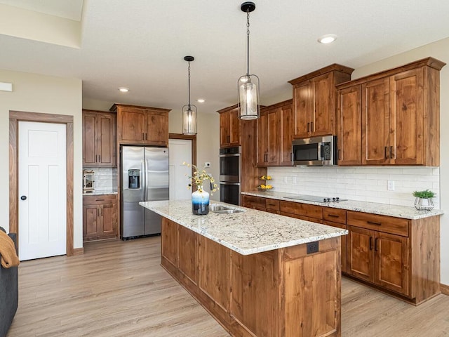 kitchen featuring pendant lighting, backsplash, an island with sink, appliances with stainless steel finishes, and light hardwood / wood-style floors