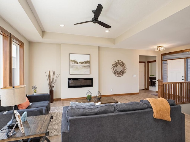 living room featuring ceiling fan, light wood-type flooring, and a tray ceiling