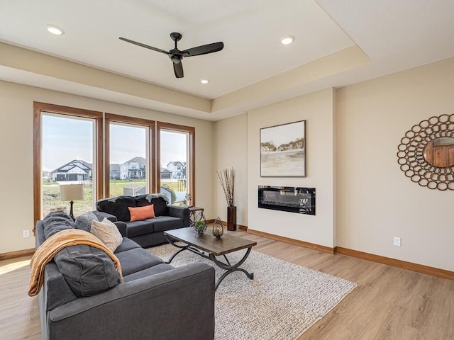 living room featuring a tray ceiling, ceiling fan, and light hardwood / wood-style flooring