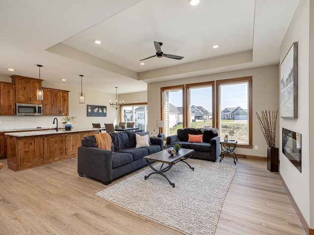 living room featuring a raised ceiling, sink, light hardwood / wood-style floors, and ceiling fan with notable chandelier