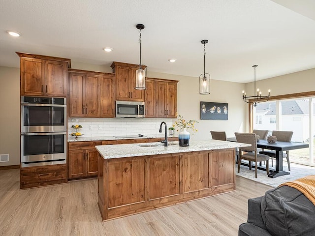 kitchen featuring tasteful backsplash, stainless steel appliances, sink, a notable chandelier, and hanging light fixtures