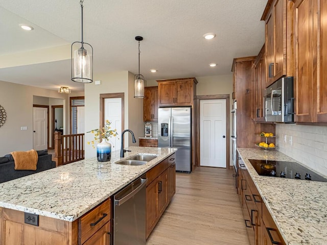 kitchen with sink, stainless steel appliances, tasteful backsplash, an island with sink, and decorative light fixtures