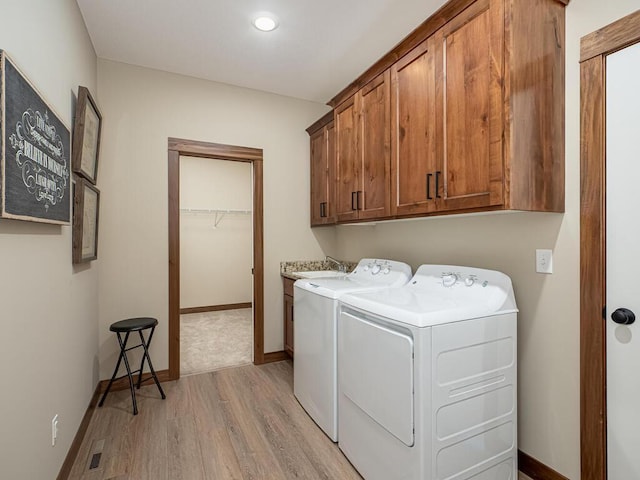 washroom with washing machine and clothes dryer, light hardwood / wood-style flooring, and cabinets