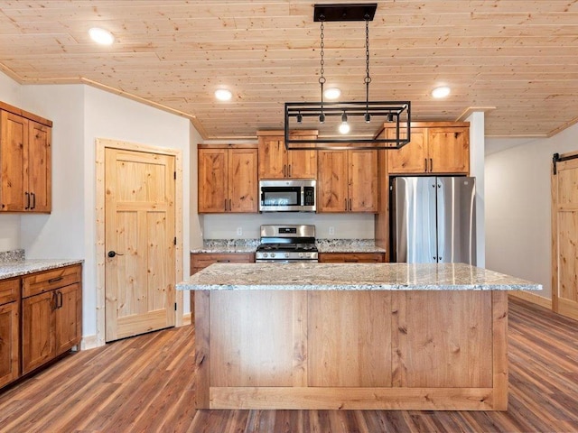 kitchen featuring a kitchen island, hanging light fixtures, a barn door, stainless steel appliances, and light stone countertops