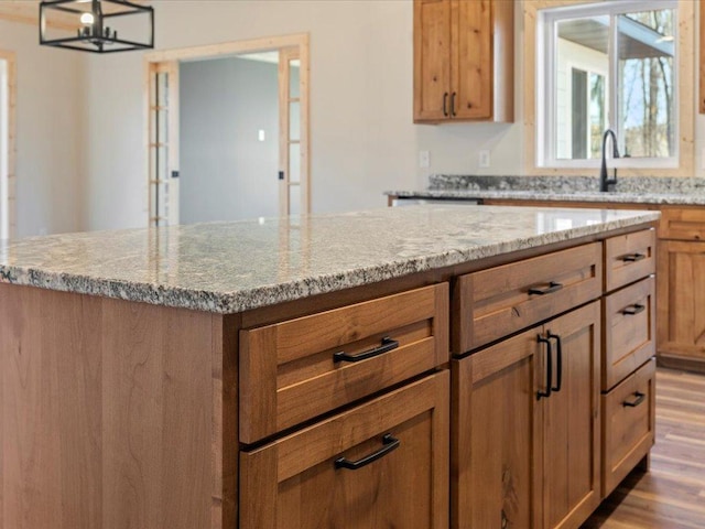 kitchen featuring hanging light fixtures, a kitchen island, light stone counters, and light hardwood / wood-style flooring