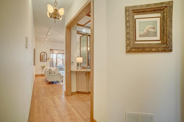 corridor with rail lighting, an inviting chandelier, and light hardwood / wood-style flooring