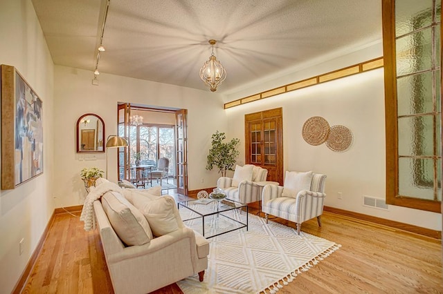 living room with an inviting chandelier, a textured ceiling, and light wood-type flooring