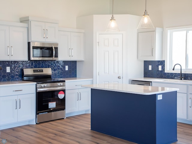 kitchen with stainless steel appliances, sink, pendant lighting, white cabinets, and a kitchen island