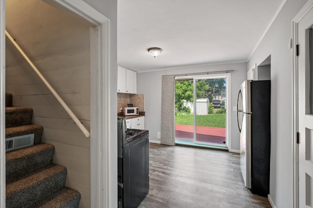 kitchen featuring black range oven, backsplash, stainless steel fridge, white cabinets, and hardwood / wood-style flooring