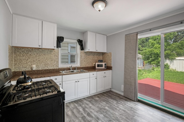 kitchen with black gas range, white cabinetry, sink, tasteful backsplash, and light hardwood / wood-style flooring