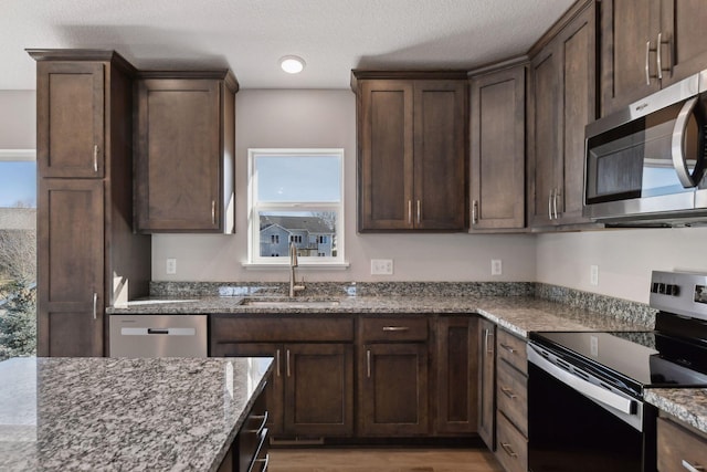 kitchen featuring appliances with stainless steel finishes, dark brown cabinetry, stone countertops, and sink