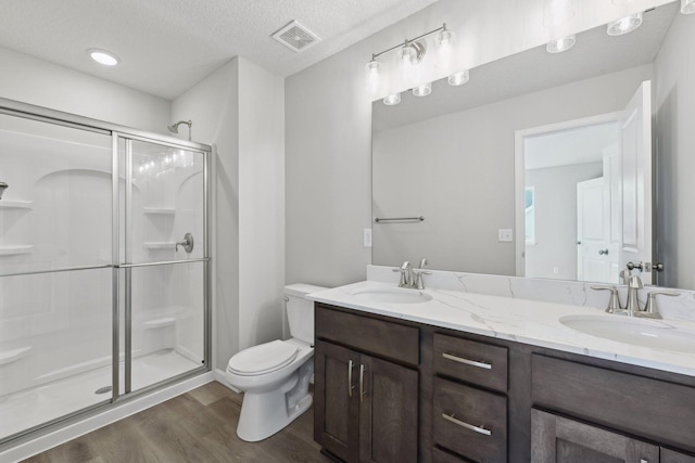 bathroom with vanity, a textured ceiling, a shower with door, hardwood / wood-style flooring, and toilet