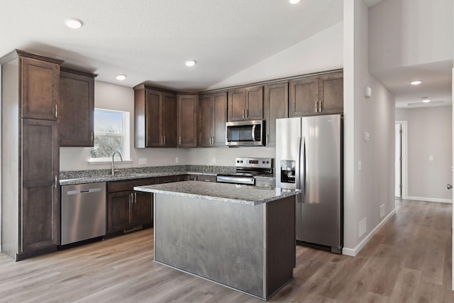 kitchen with dark brown cabinetry, a center island, stainless steel appliances, light stone counters, and lofted ceiling