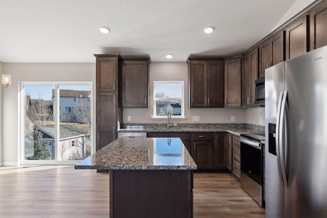 kitchen featuring appliances with stainless steel finishes, dark stone counters, dark brown cabinets, sink, and a kitchen island