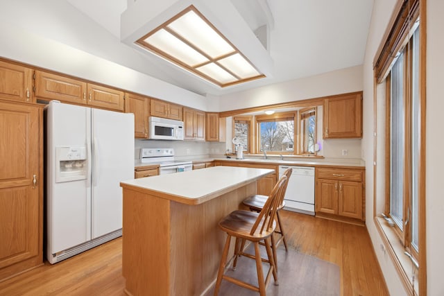 kitchen featuring sink, white appliances, a kitchen breakfast bar, light hardwood / wood-style flooring, and a kitchen island