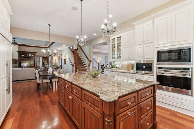 kitchen with white cabinets, black microwave, hanging light fixtures, a kitchen island with sink, and stainless steel oven