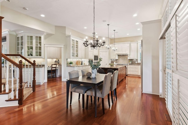 dining space with dark wood-type flooring, crown molding, and an inviting chandelier