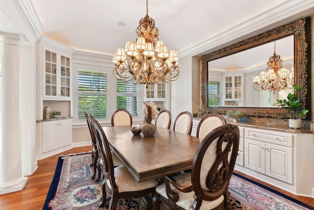 dining area featuring light wood-type flooring, ornate columns, ornamental molding, and a notable chandelier