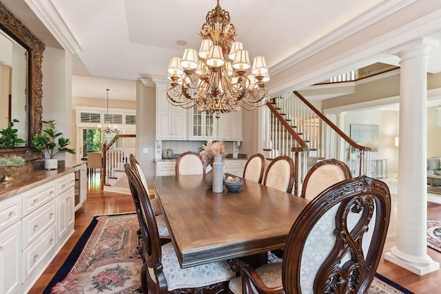 dining space with ornate columns, an inviting chandelier, hardwood / wood-style floors, a tray ceiling, and ornamental molding