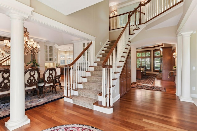 stairs with an inviting chandelier, ornate columns, a towering ceiling, and hardwood / wood-style flooring