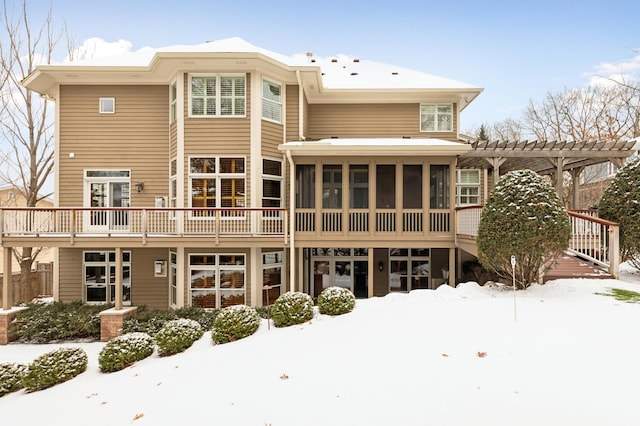 snow covered back of property featuring a deck, a sunroom, and a pergola