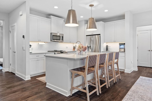 kitchen featuring white cabinets, pendant lighting, stainless steel appliances, and an island with sink