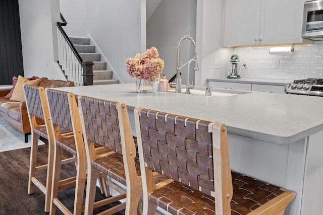 kitchen with sink, tasteful backsplash, dark hardwood / wood-style flooring, a breakfast bar, and white cabinets