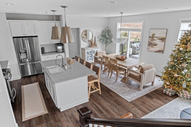 kitchen with sink, decorative light fixtures, a center island with sink, stainless steel fridge with ice dispenser, and white cabinetry