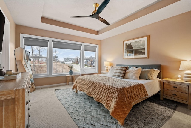 carpeted bedroom with a tray ceiling and ceiling fan