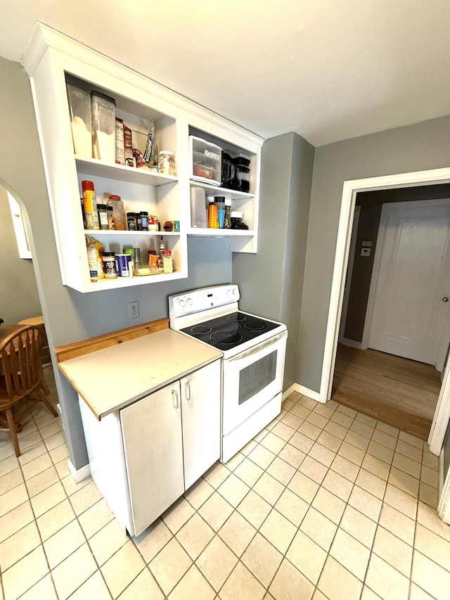 kitchen with white electric stove, light tile patterned floors, and white cabinetry