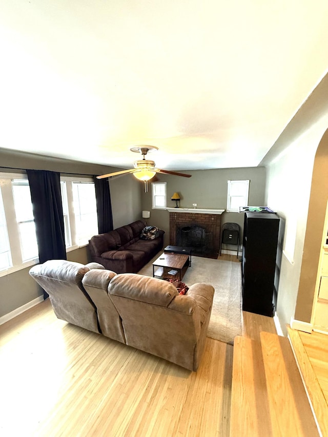 living room with a fireplace, light wood-type flooring, and ceiling fan