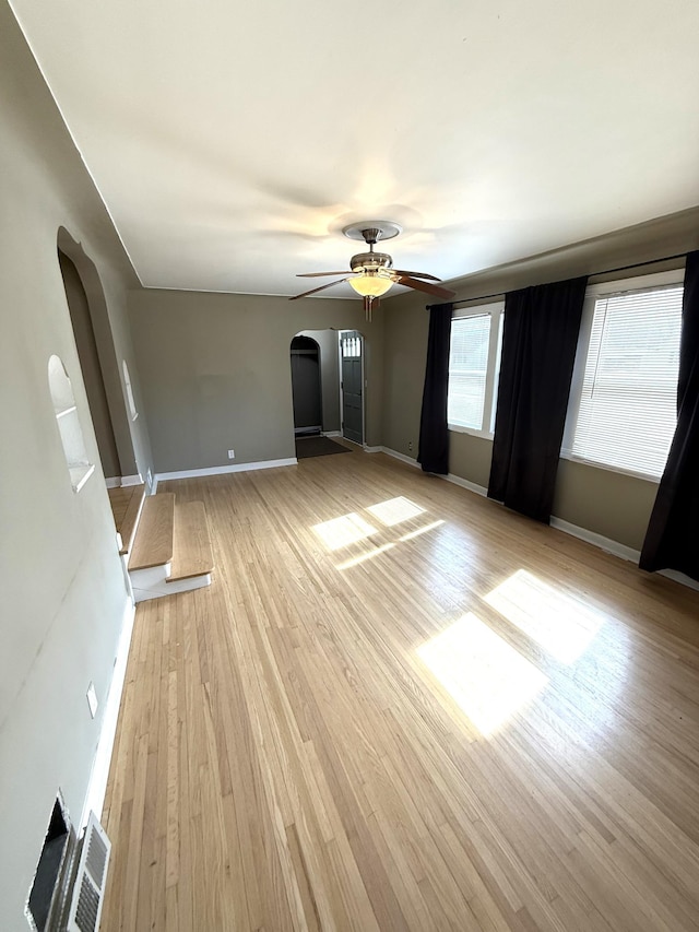 interior space with a ceiling fan, baseboards, visible vents, arched walkways, and light wood-type flooring