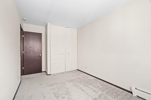 unfurnished bedroom featuring a closet, light colored carpet, and baseboard heating