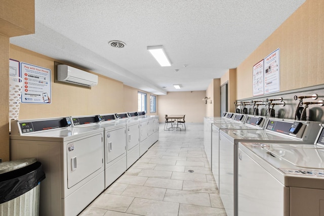 laundry area with washing machine and dryer, an AC wall unit, a textured ceiling, and light tile patterned floors