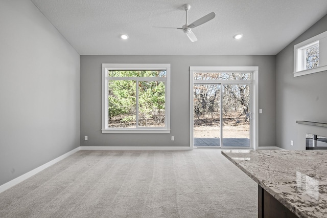 unfurnished living room with ceiling fan, light colored carpet, a textured ceiling, and vaulted ceiling