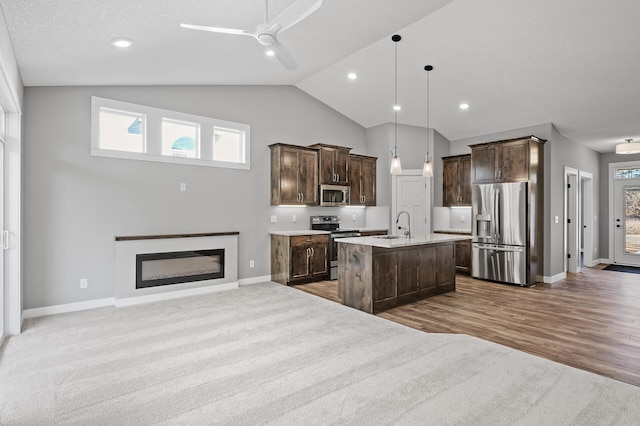 kitchen with appliances with stainless steel finishes, dark brown cabinets, ceiling fan, decorative light fixtures, and an island with sink