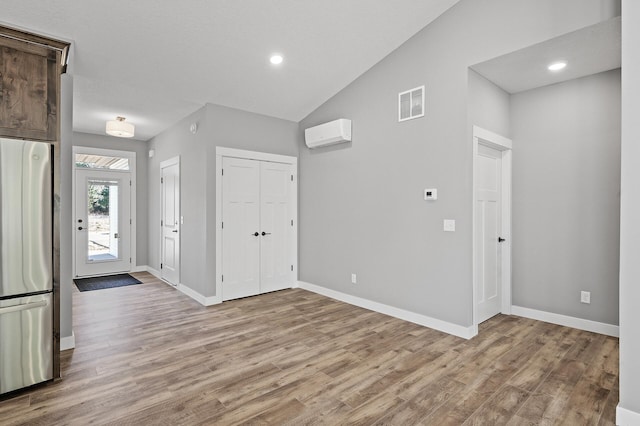 entrance foyer with a wall mounted air conditioner, light hardwood / wood-style floors, and lofted ceiling