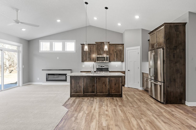 kitchen with ceiling fan, an island with sink, appliances with stainless steel finishes, decorative light fixtures, and dark brown cabinets